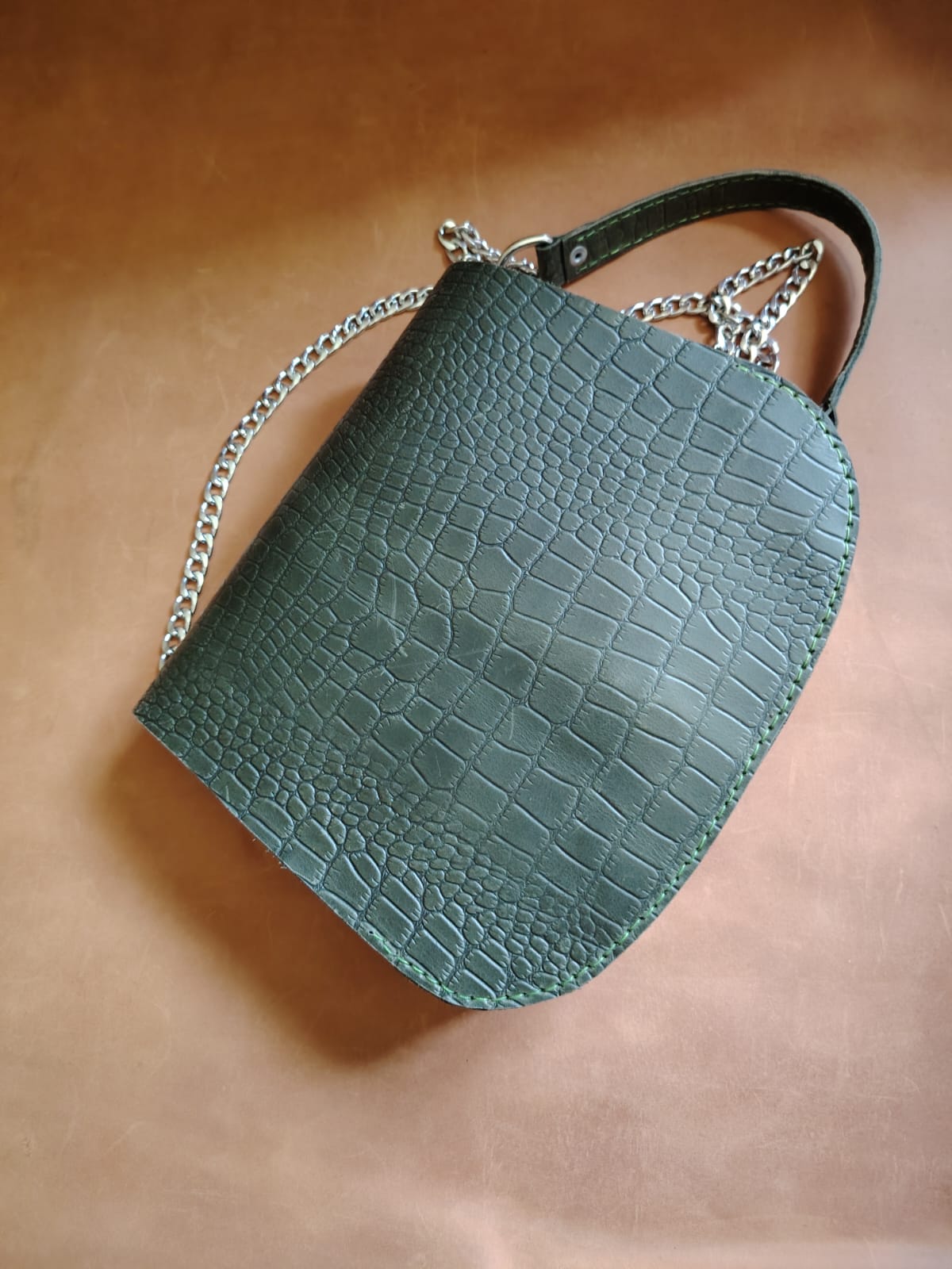 Green crocodile-textured handbag with a chain strap on a beige background